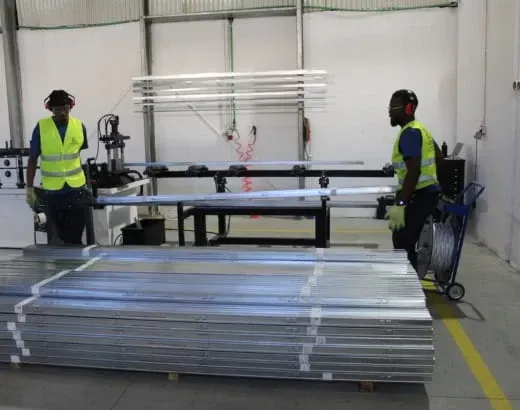 Dois operários com coletes de segurança manuseando grandes painéis de metal em um armazém.