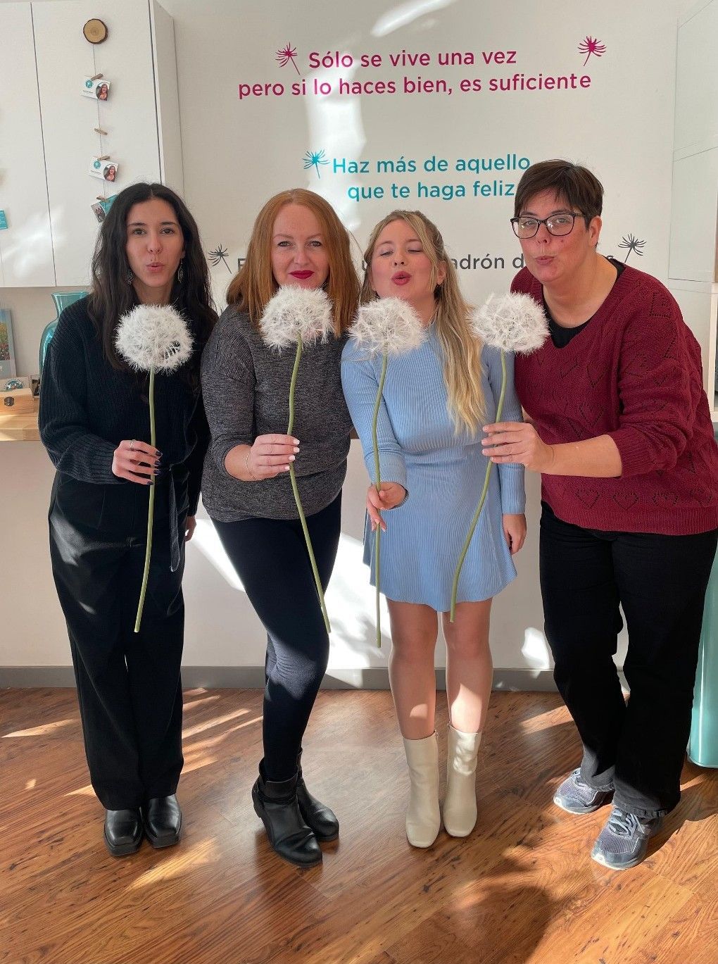 Un grupo de mujeres están paradas una al lado de la otra sosteniendo dientes de león.