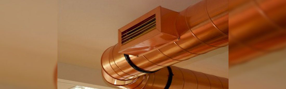 Un conducto de aire cilíndrico, de metal, de color cobre, suspendido de un techo con un respiradero rectangular que sobresale de su costado.