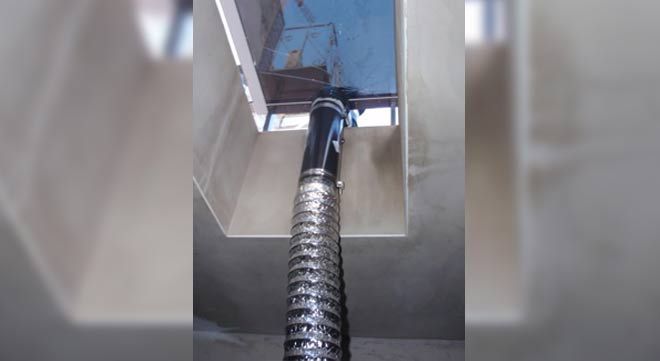 Una manguera de ventilación de metal flexible se extiende hacia arriba dentro de una abertura rectangular en el techo.