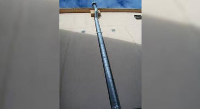 Un tubo de ventilación de metal vertical montado contra una pared exterior utilizando un espaciador de bloque de madera debajo de la línea del techo.