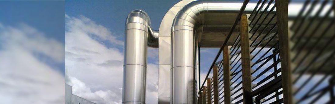Grandes tubos metálicos con revestimiento plateado aislante se elevan contra un cielo azul nublado.