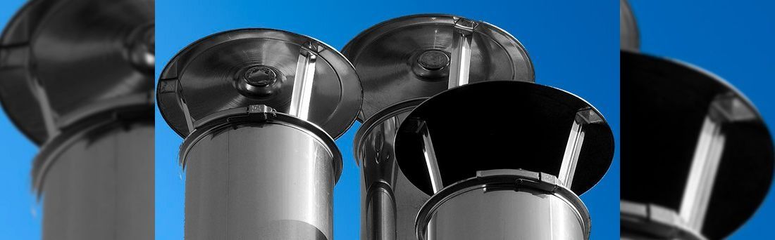 Varios tubos de chimenea de metal con tapas redondas contra un cielo azul brillante.