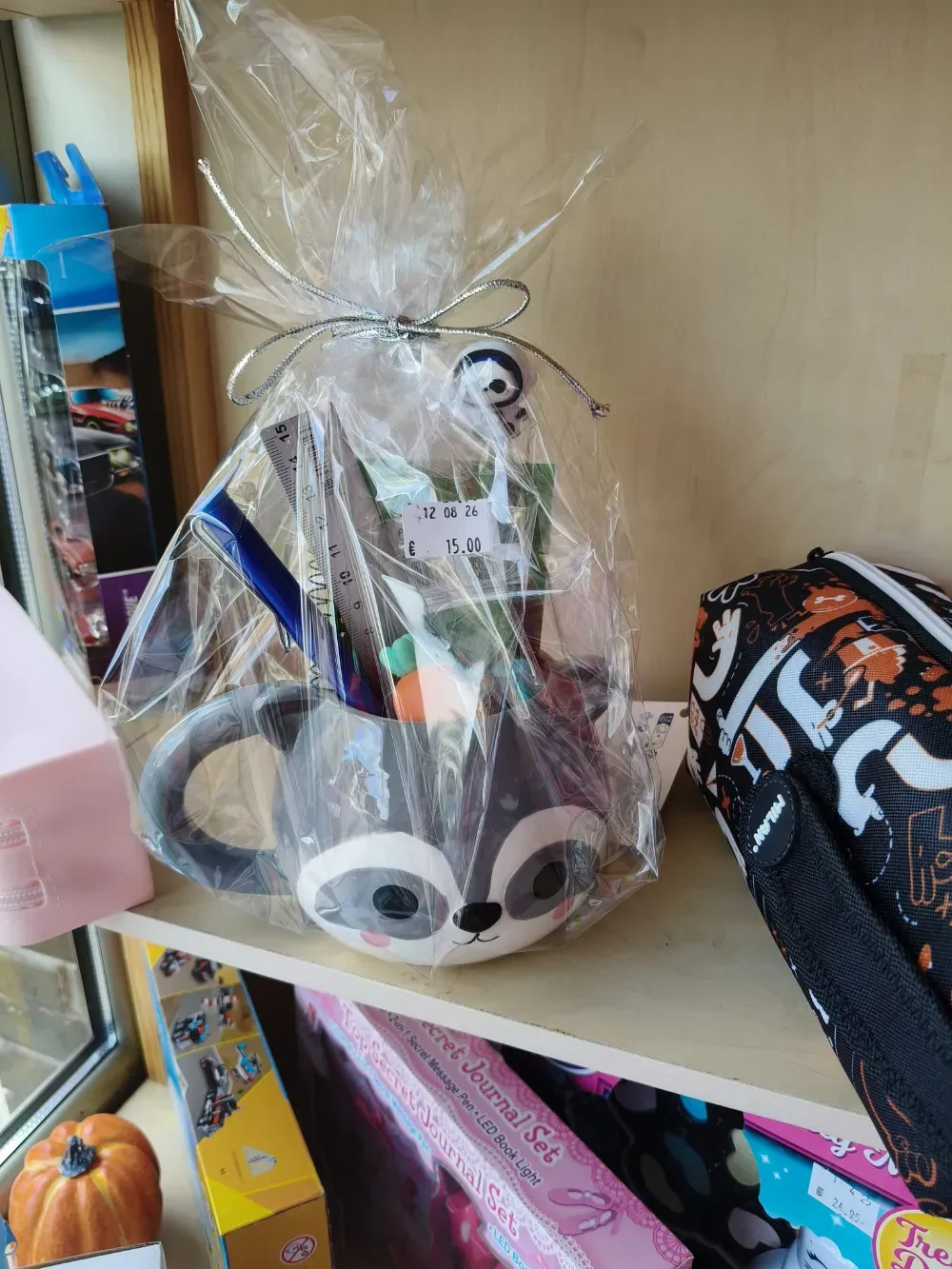 Bolsa de regalo transparente con un peluche sobre una estantería de madera, junto a una bolsa negra estampada.