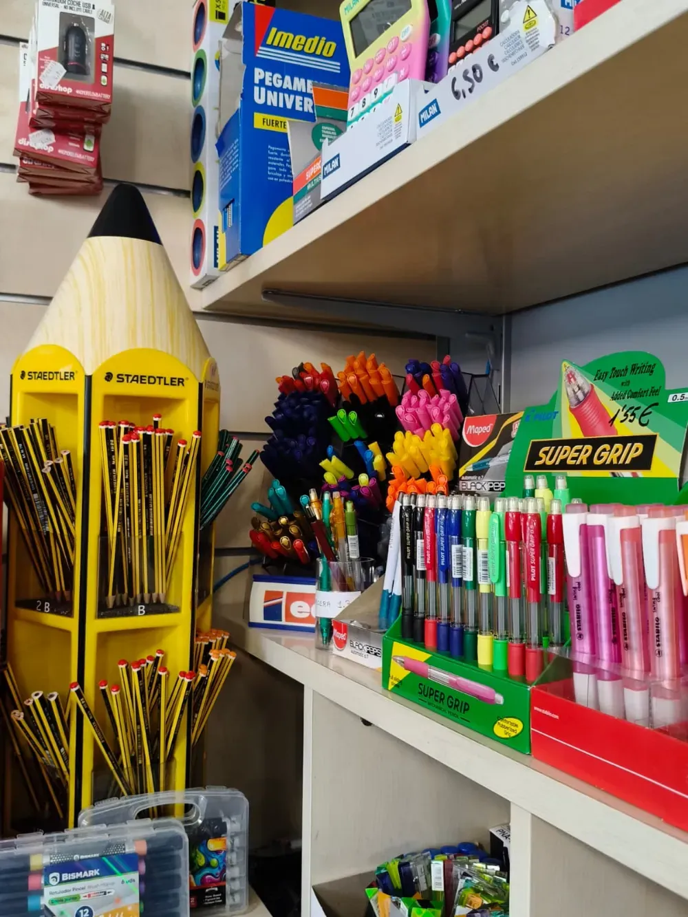 Estante de tienda con material escolar de colores, lápices, bolígrafos, rotuladores y lápices de gran tamaño en exhibición