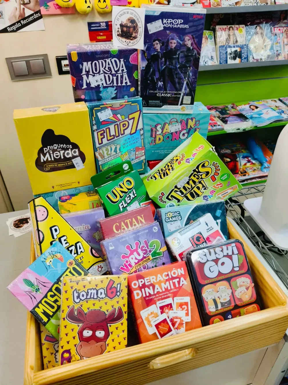 Expositor colorido de juegos de mesa en una cesta de tienda, con UNO, Catan, Flip 7 y otros juegos