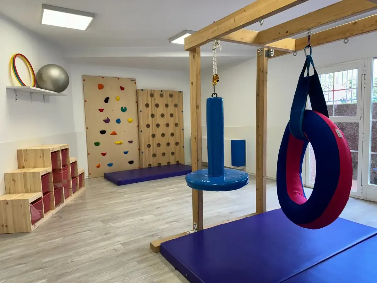 Sala de juegos con piso de madera clara, paredes azules y blancas, ventanas grandes y tres juguetes mecedores.