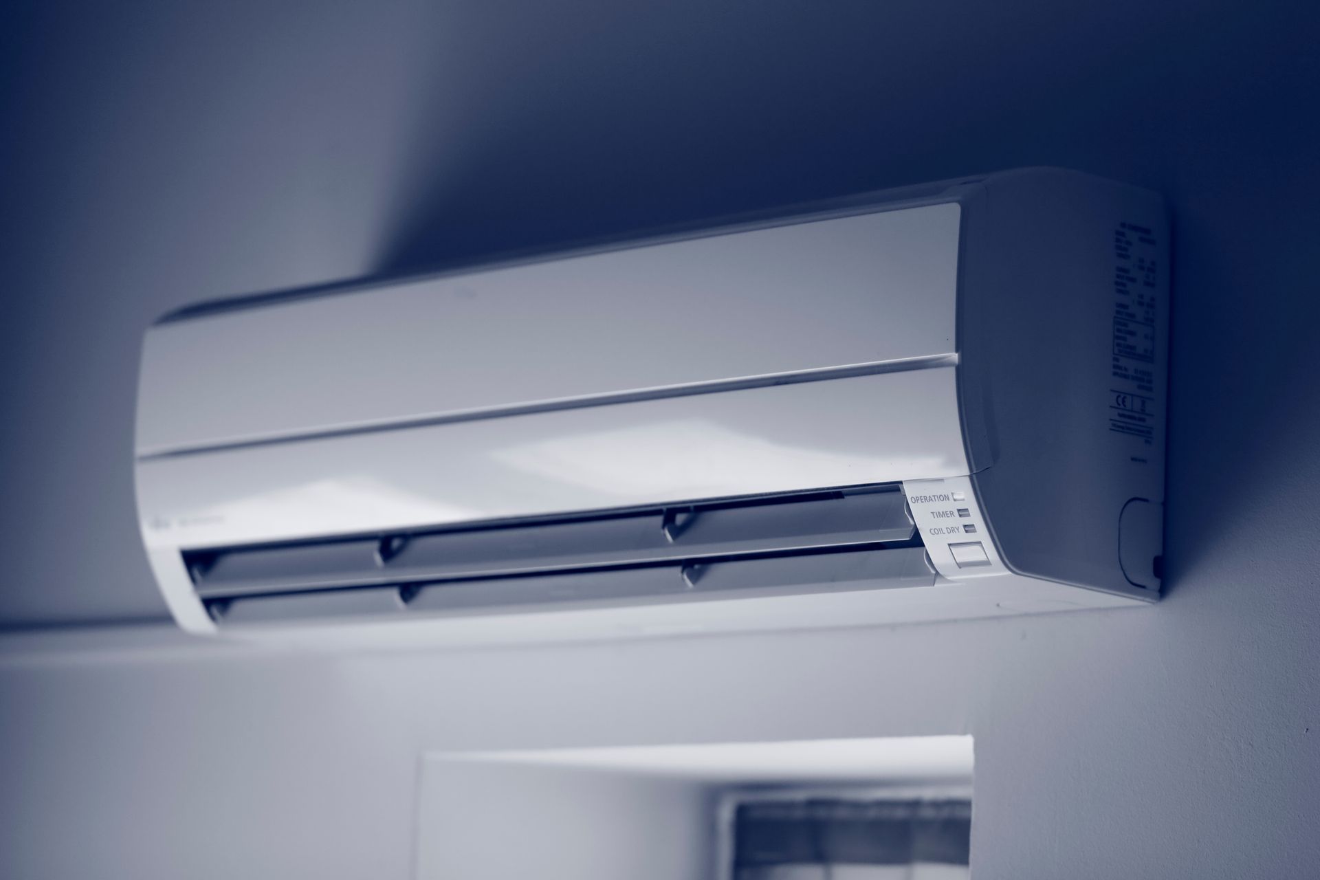 Unité de climatisation murale blanche avec des grilles d'aération noires, fixée sur un mur bleu clair.