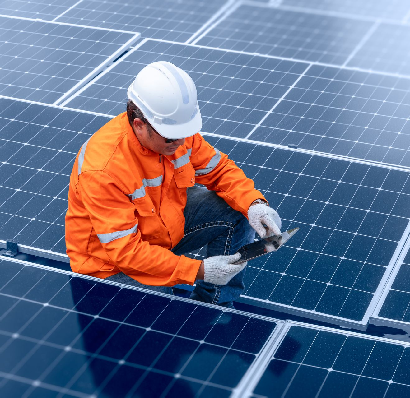 Technicien de panneaux solaires en combinaison orange, casque et gants blancs, examinant des panneaux.