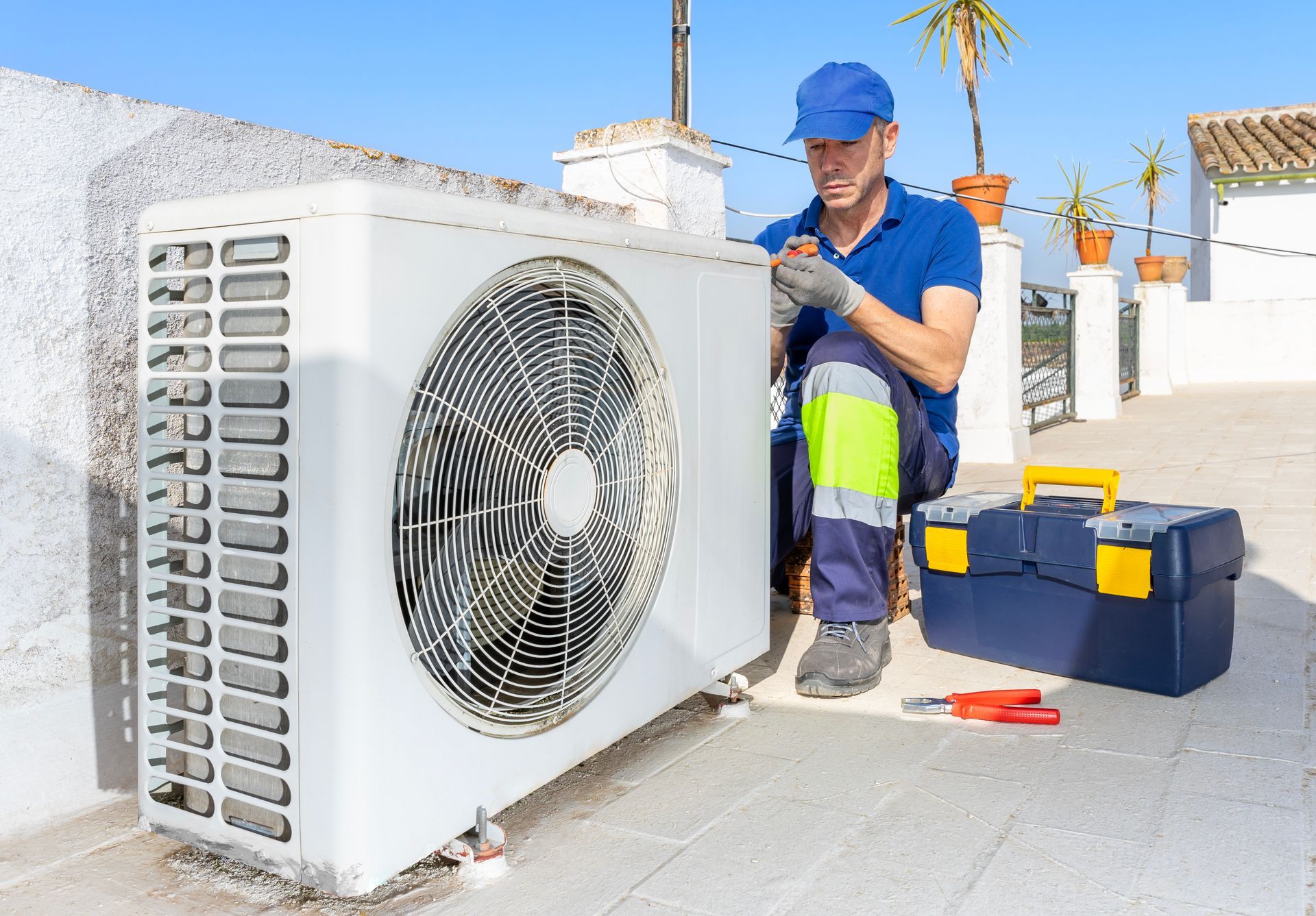 Technicien CVC en chemise bleue et casquette en train d'entretenir un climatiseur sur un toit.