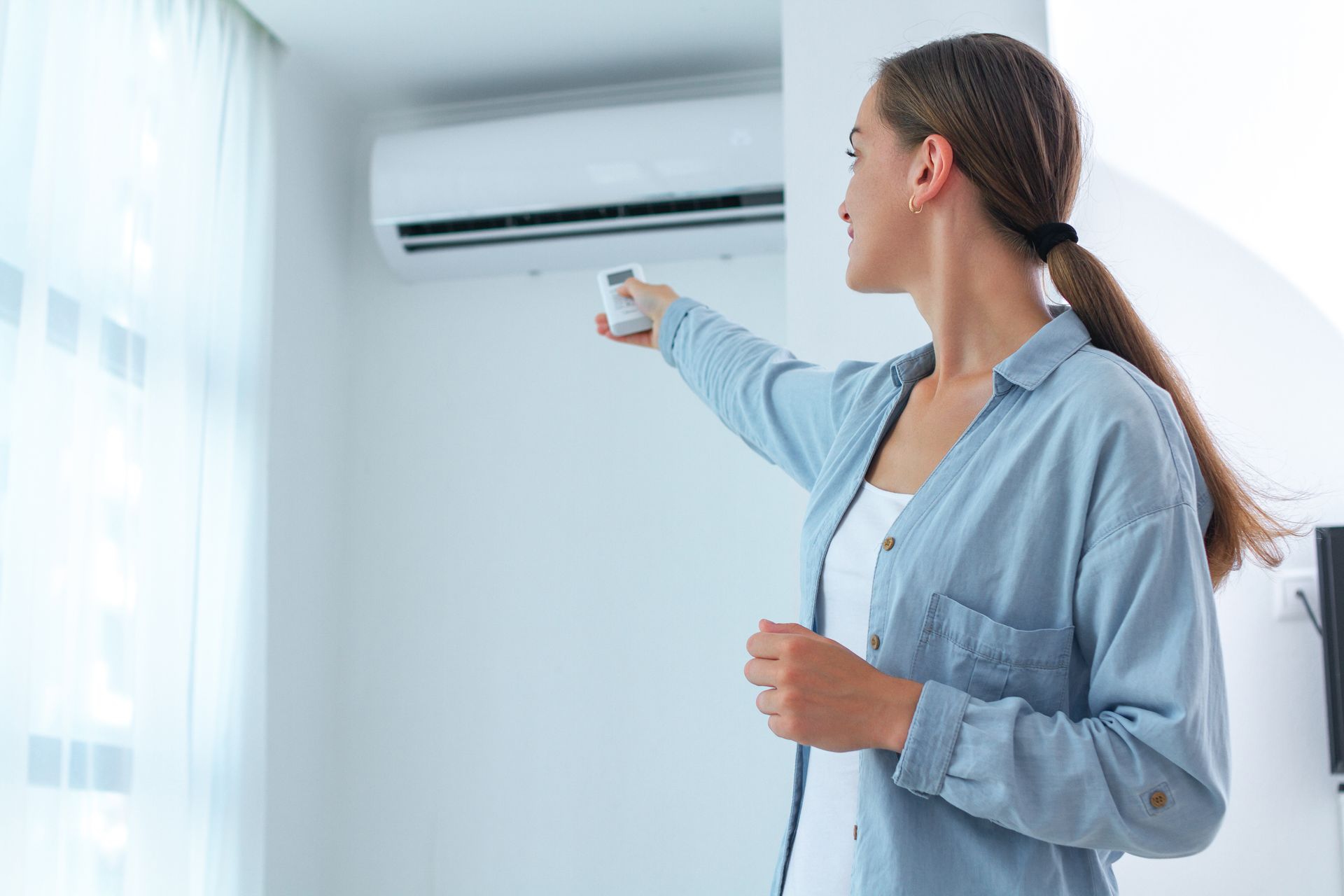 Une femme utilise une télécommande pour faire fonctionner un climatiseur blanc fixé sur un mur blanc.