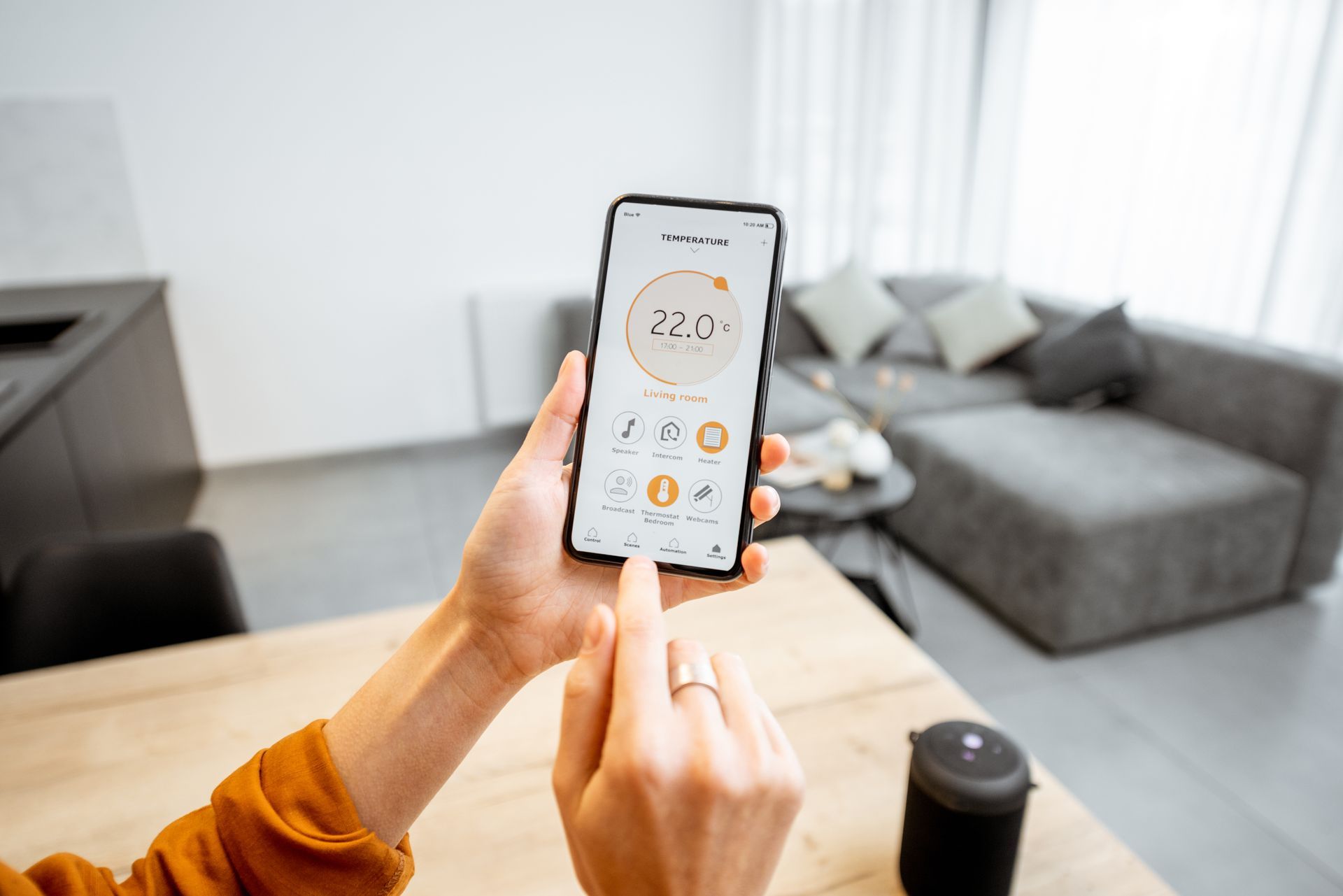 Une personne utilise un smartphone pour régler le thermostat dans un salon moderne.
