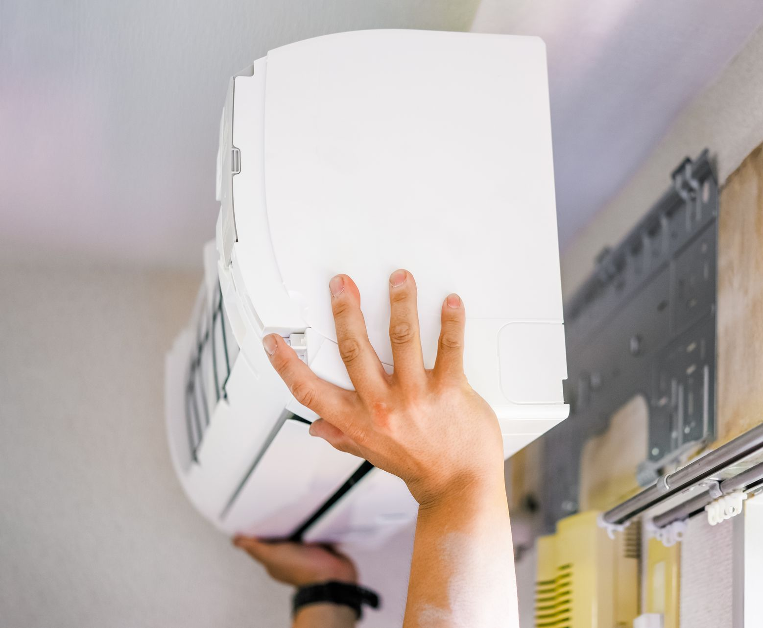 Une personne installe un climatiseur blanc sur un mur, les mains le tenant.