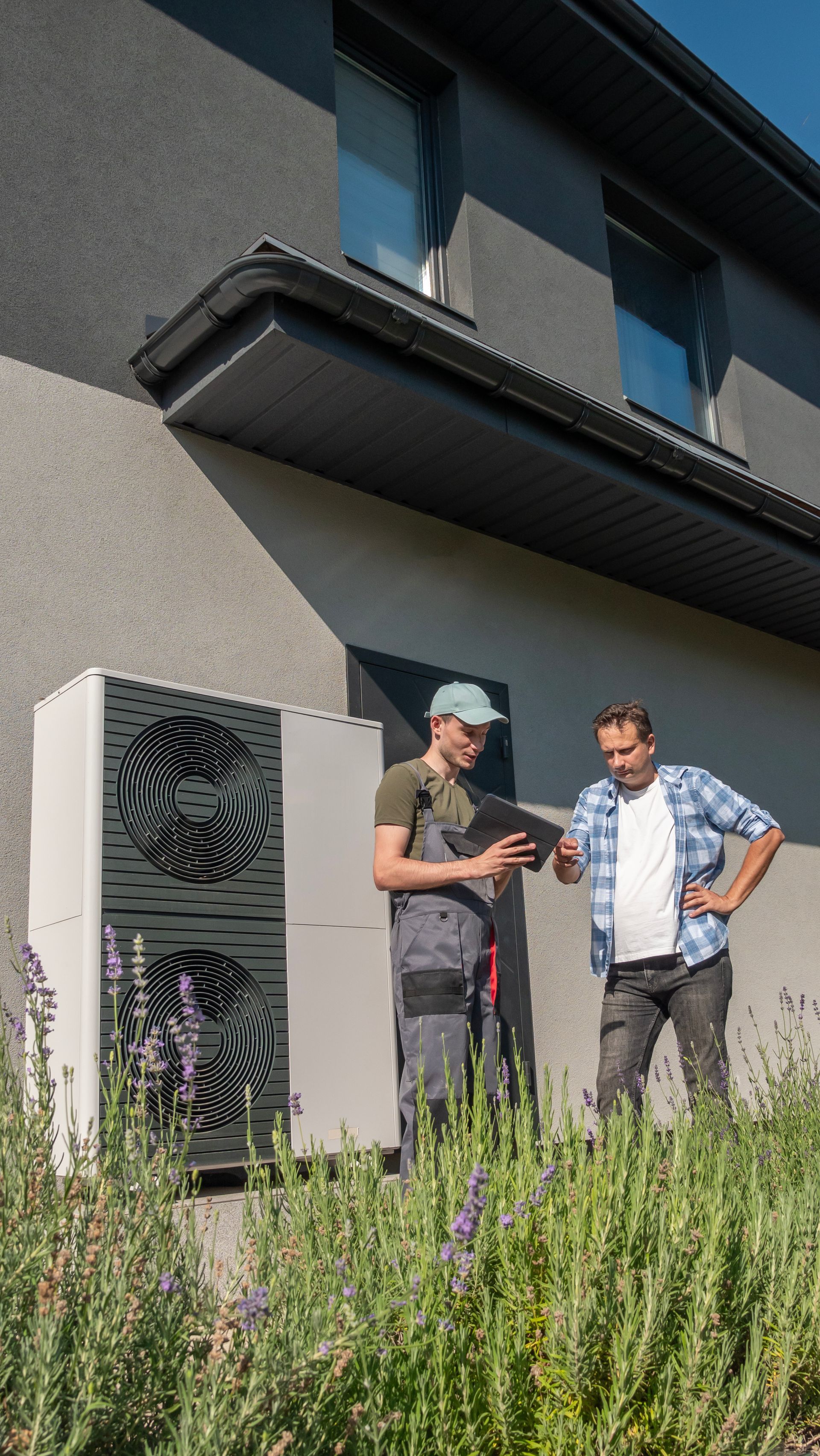Deux hommes examinent une tablette à côté d'une pompe à chaleur à l'extérieur d'une maison.