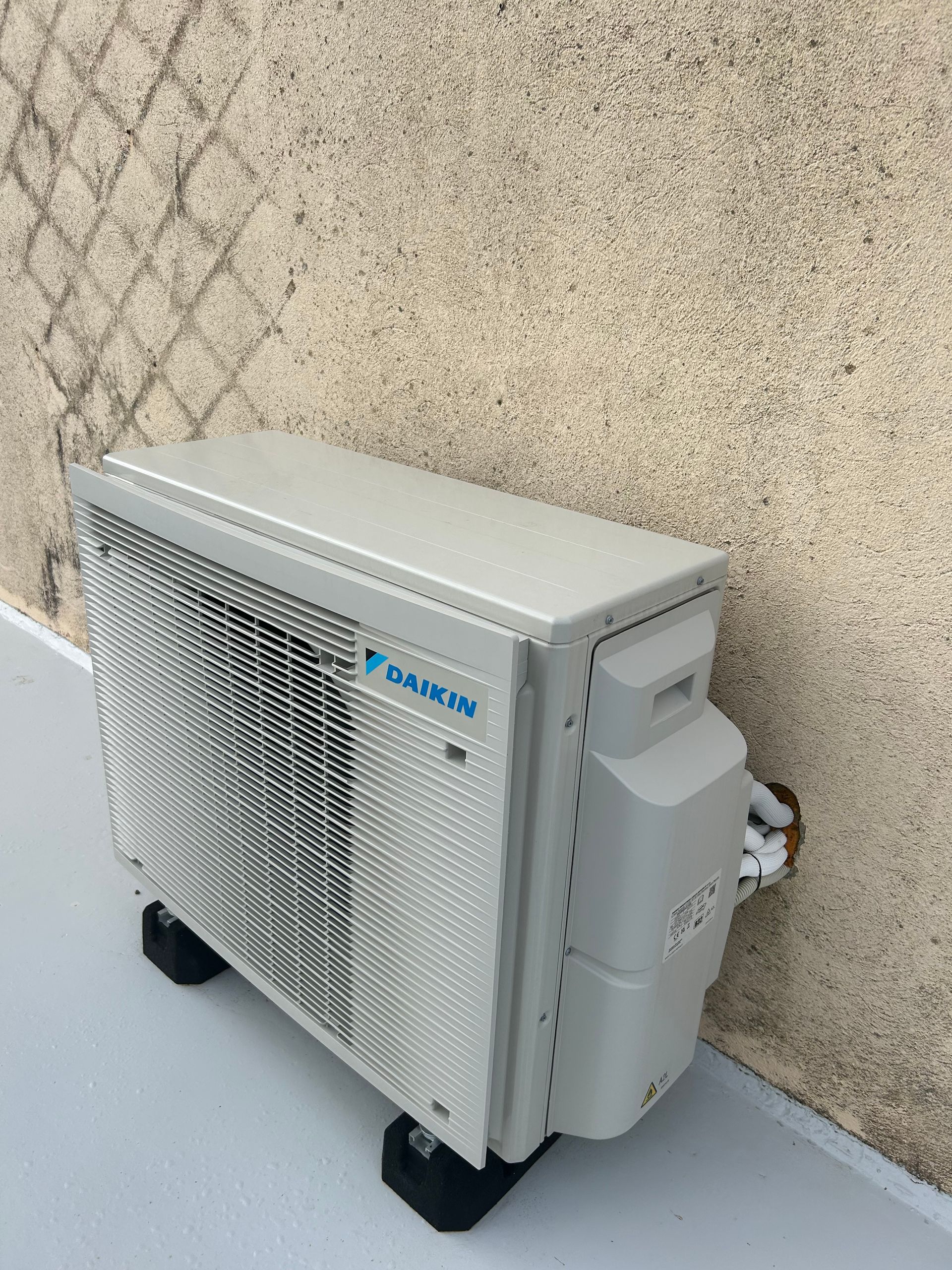 Unité de climatisation Daikin sur blocs noirs, contre un mur clair.