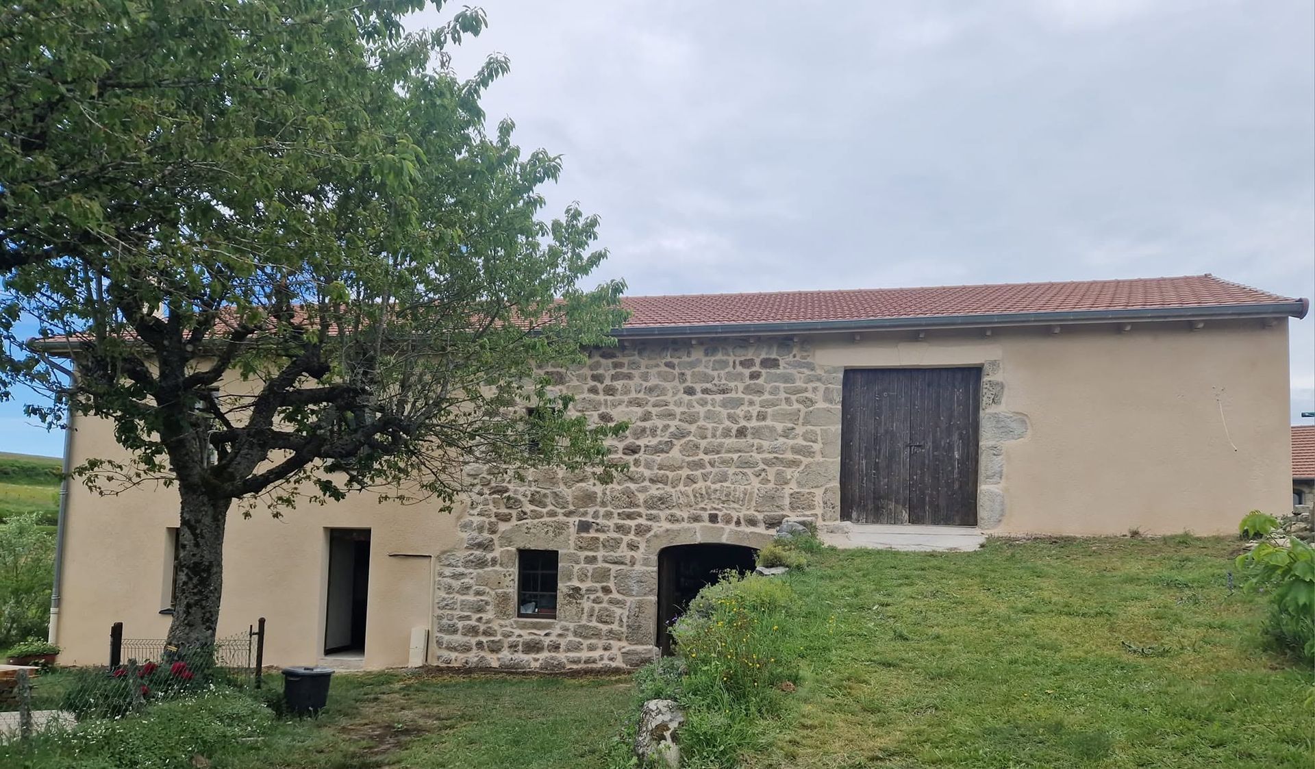 Mas en pierre au toit de tuiles rouges, près d'un arbre et d'une colline herbeuse sous un ciel nuageux