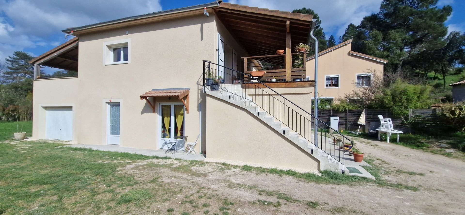 Maison beige à deux étages avec un escalier extérieur et un balcon couvert dans une cour rurale