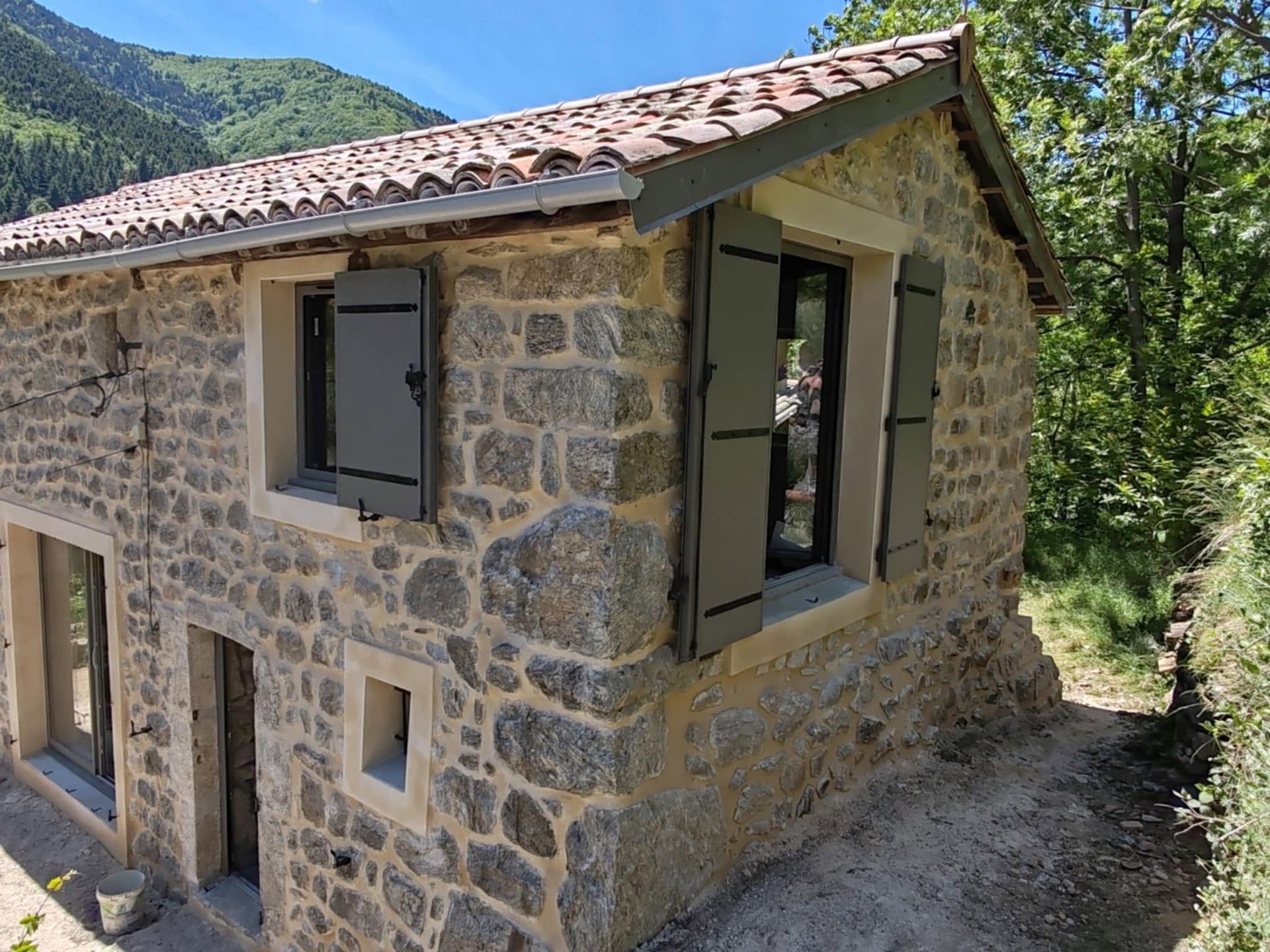 Maison en pierre avec un toit de tuiles et des fenêtres ouvertes dans un cadre montagneux boisé