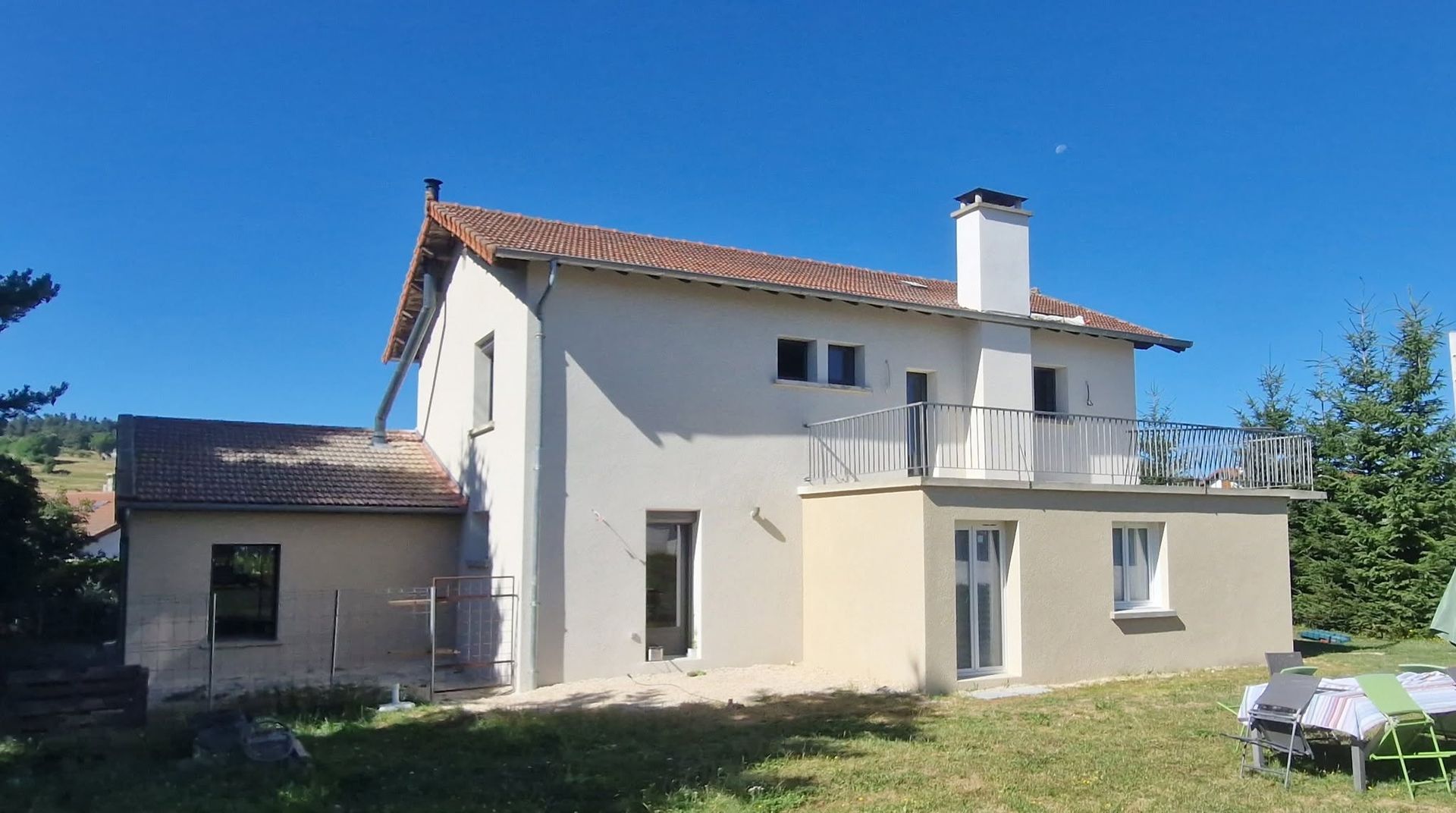Maison blanche à deux étages avec un toit de tuiles rouges et une petite terrasse avec un espace gazonné
