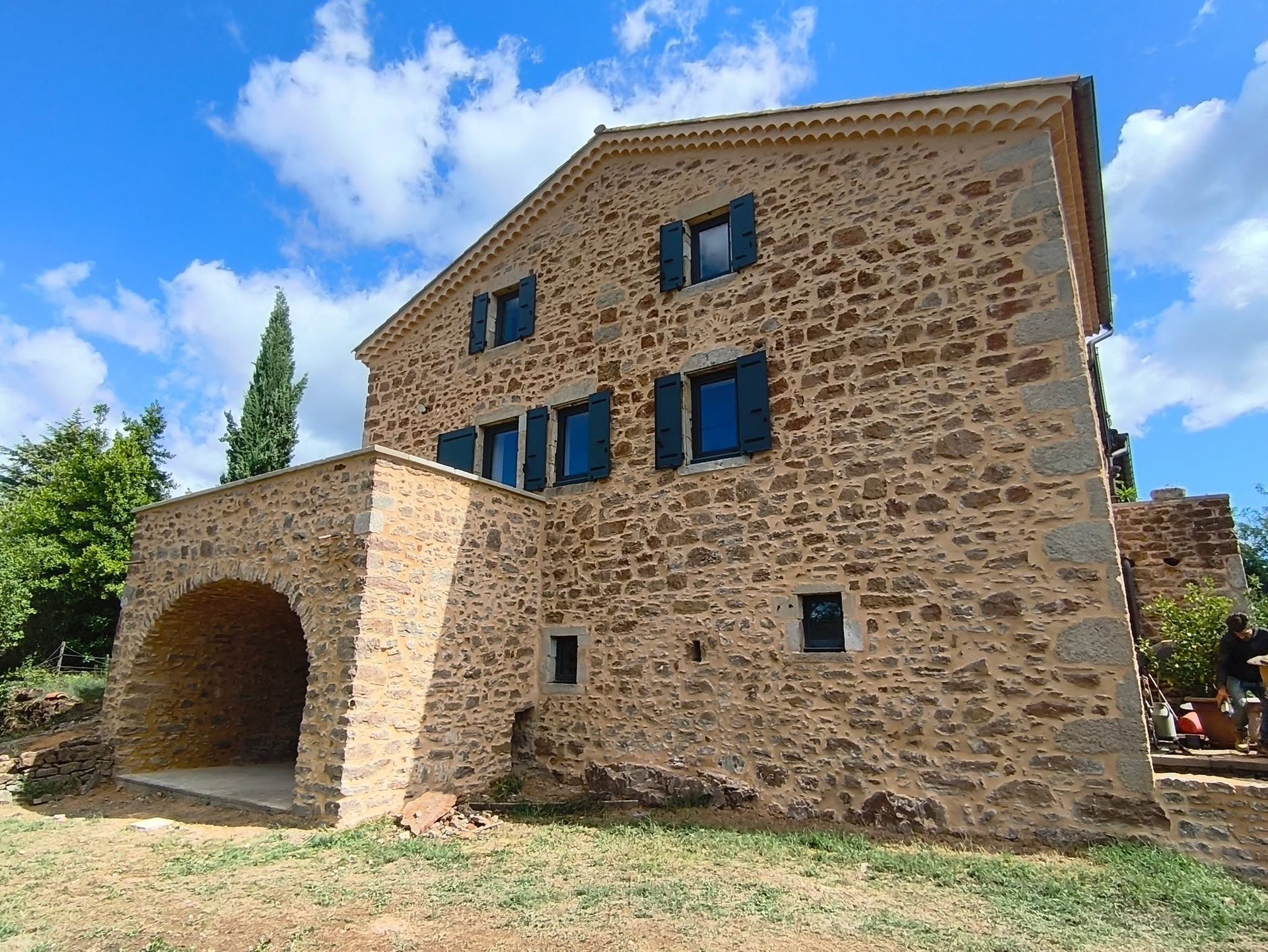 Bâtiment en pierre avec des volets bleus et une entrée voûtée sous un ciel d'un bleu éclatant