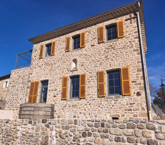 Maison en pierre avec des volets en bois et un mur en pierre sous un ciel bleu clair