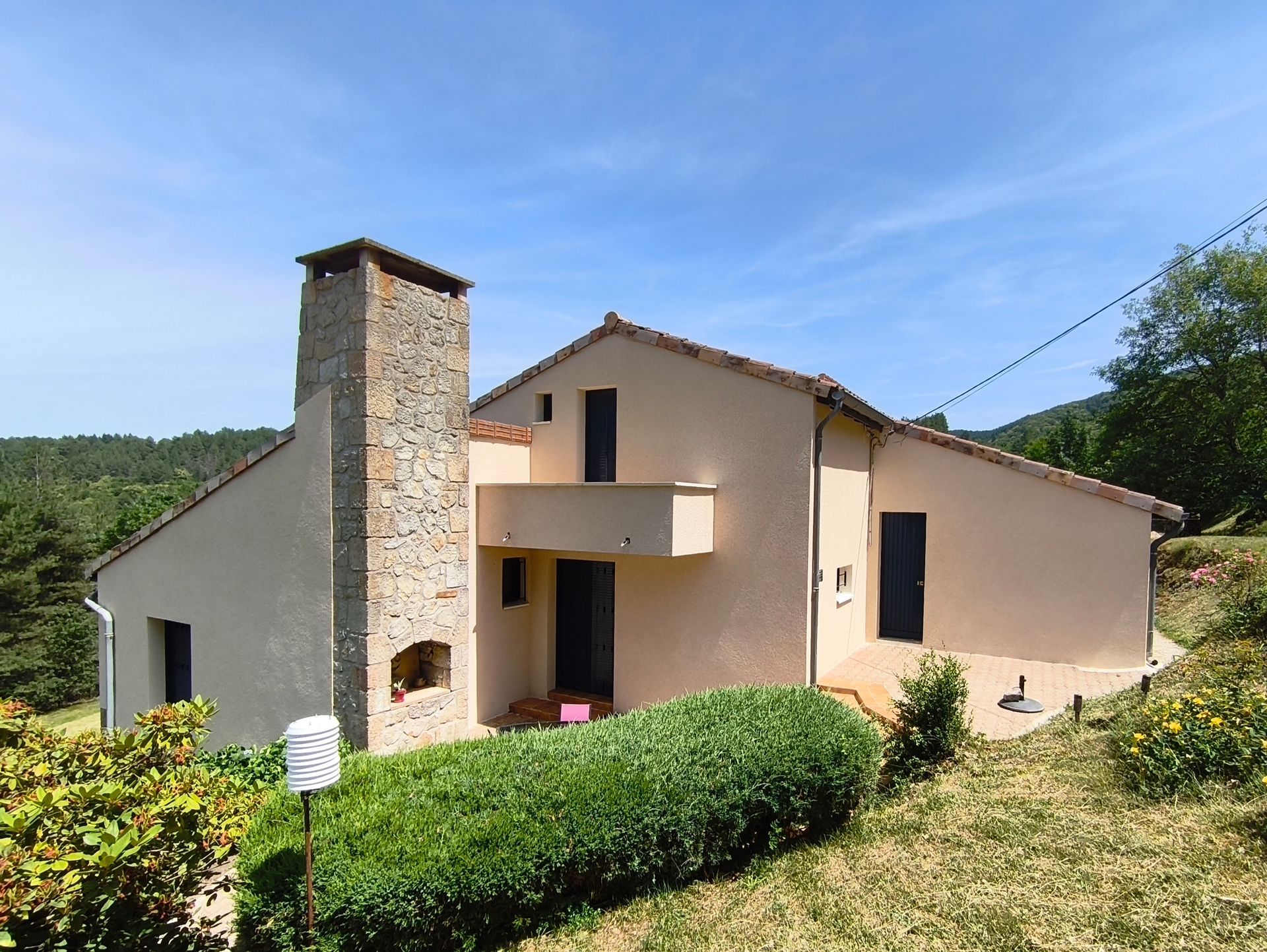 Maison beige de plain-pied avec une cheminée en pierre, des haies sous un ciel bleu