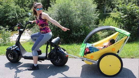 Frau auf Moped mit Baby-Anhänger