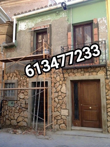 Fachada de una casa de dos plantas con muros inferiores de piedra, muros superiores verdes y andamios junto a la entrada.