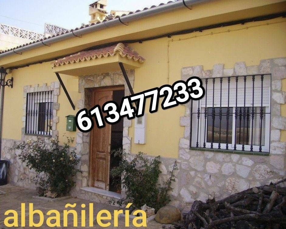 Casa amarilla con ventanas enrejadas, base de piedra y porche delantero;
