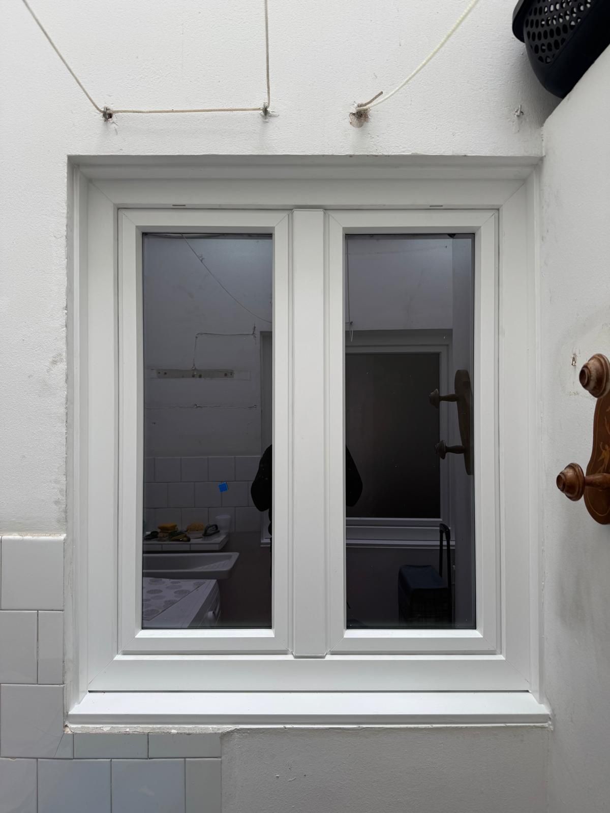 Ventana blanca de doble hoja en una pared interior beige, que muestra una calle y un edificio en el exterior.