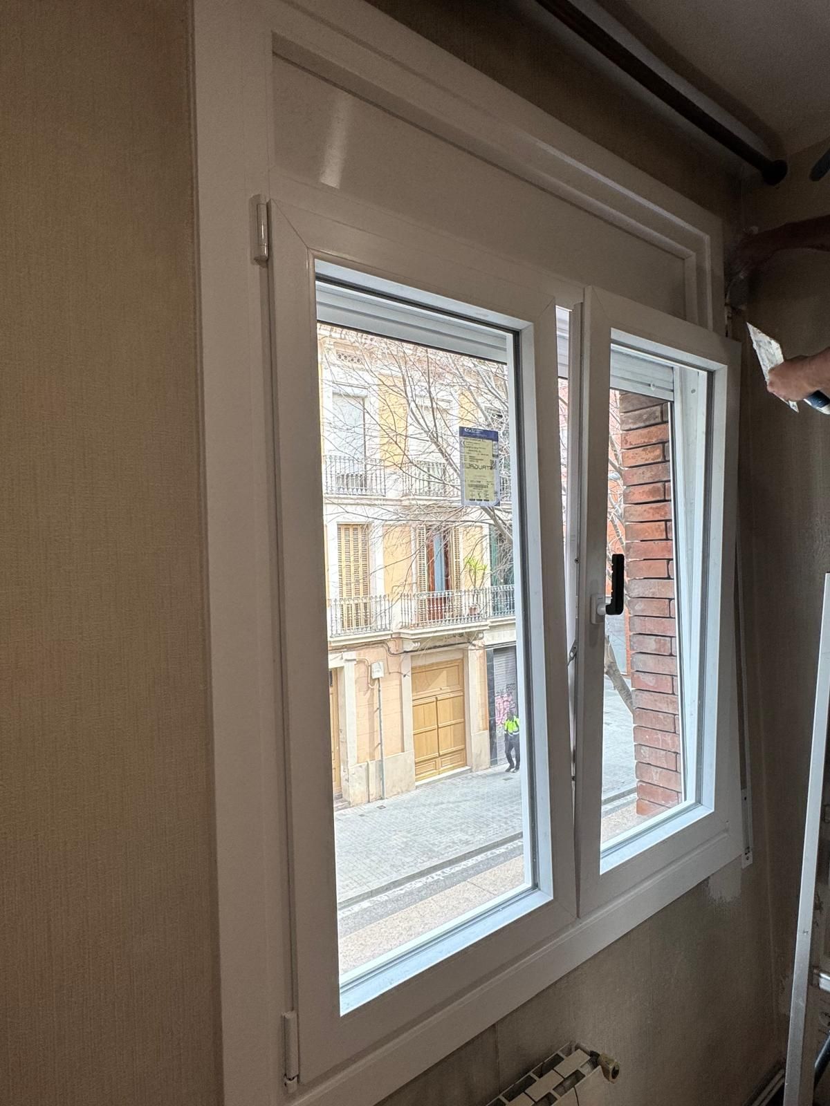 Ventana con marco blanco en una pared beige, que ofrece una vista de la calle.