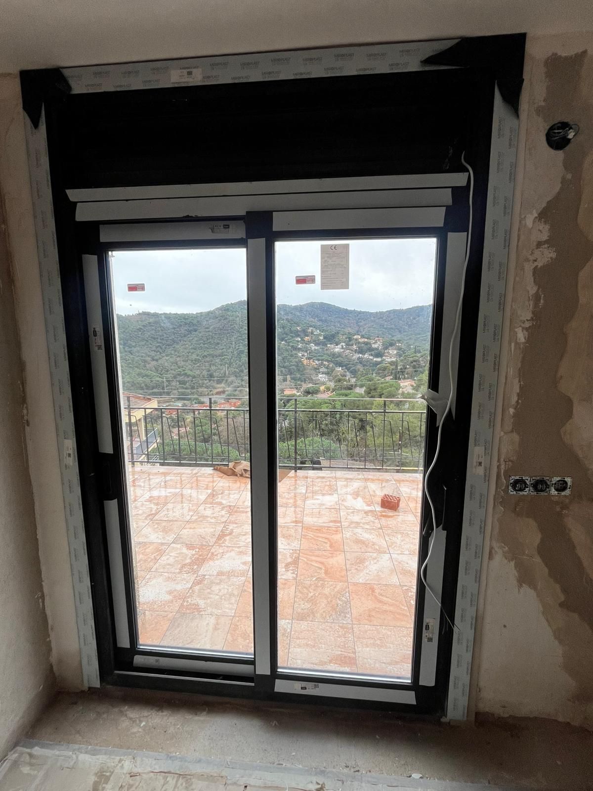 Puertas corredizas de cristal que dan a un balcón con baldosas y vistas a la ladera.