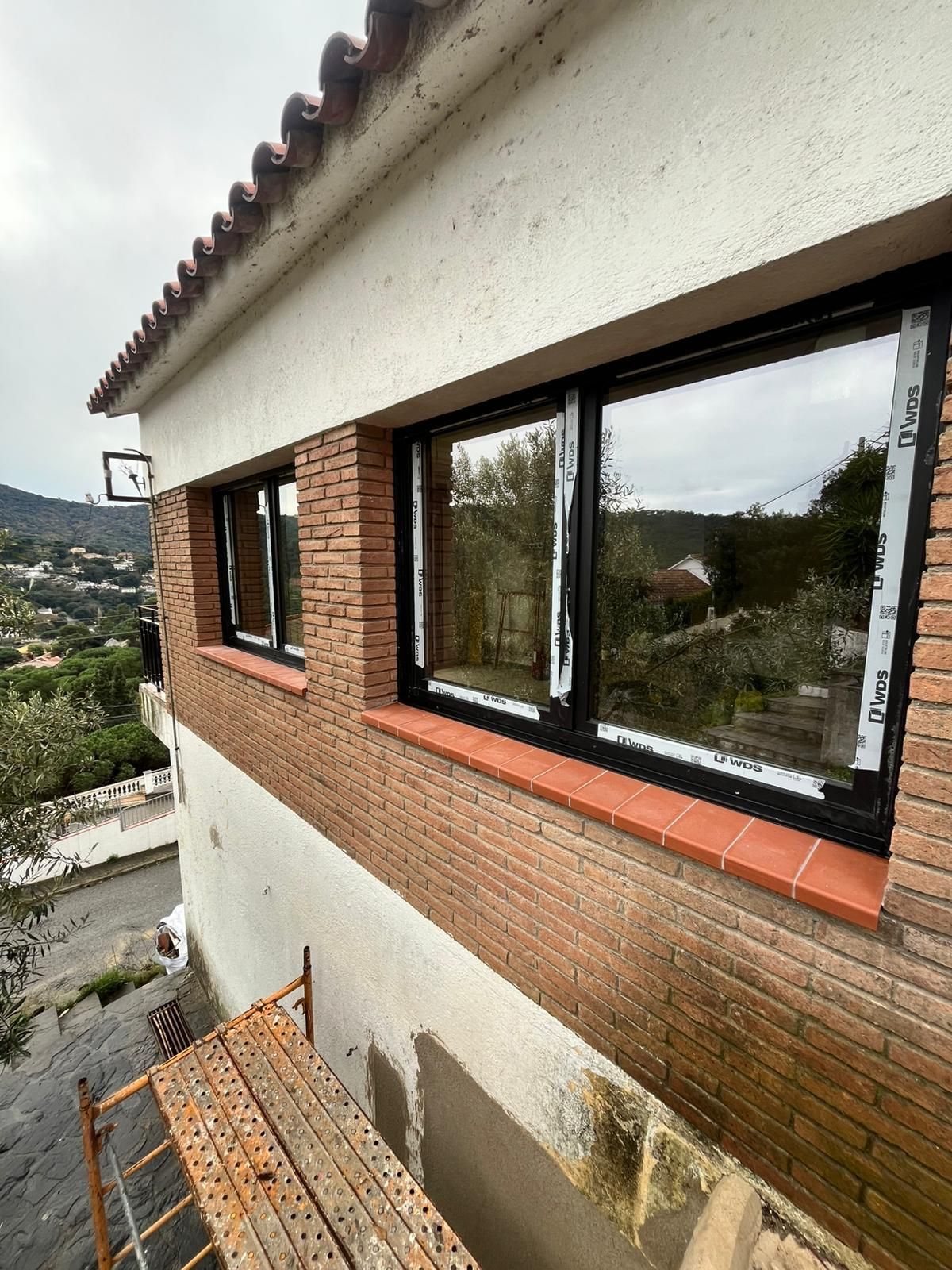 Pared sin terminar con un pequeño marco de ventana de doble acristalamiento instalado, rodeada de molduras y yeso a la vista.