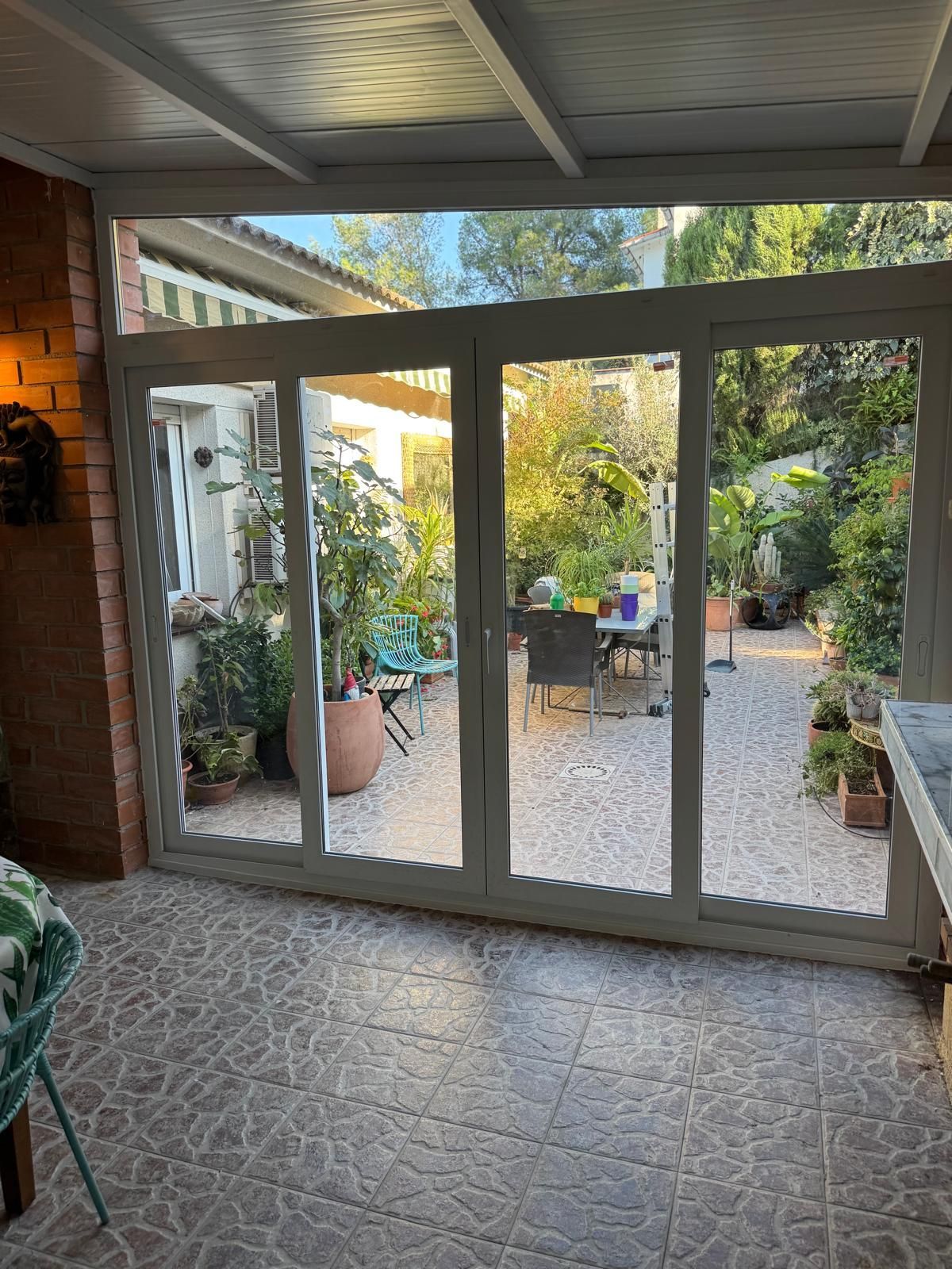 Un luminoso solárium con paredes de cristal, plantas en macetas y una mesa redonda bajo un techo blanco curvo.