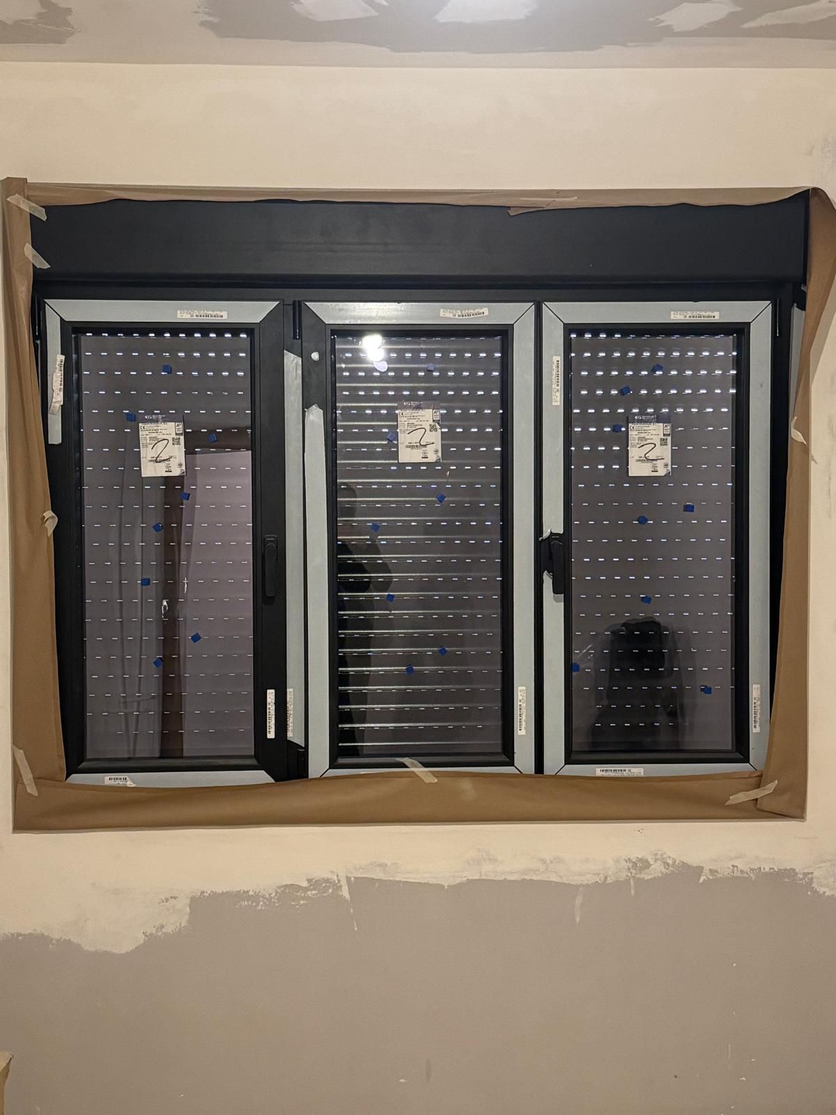 Pared exterior blanca con una ventana de marco negro y un pequeño armario de madera montado a su lado.
