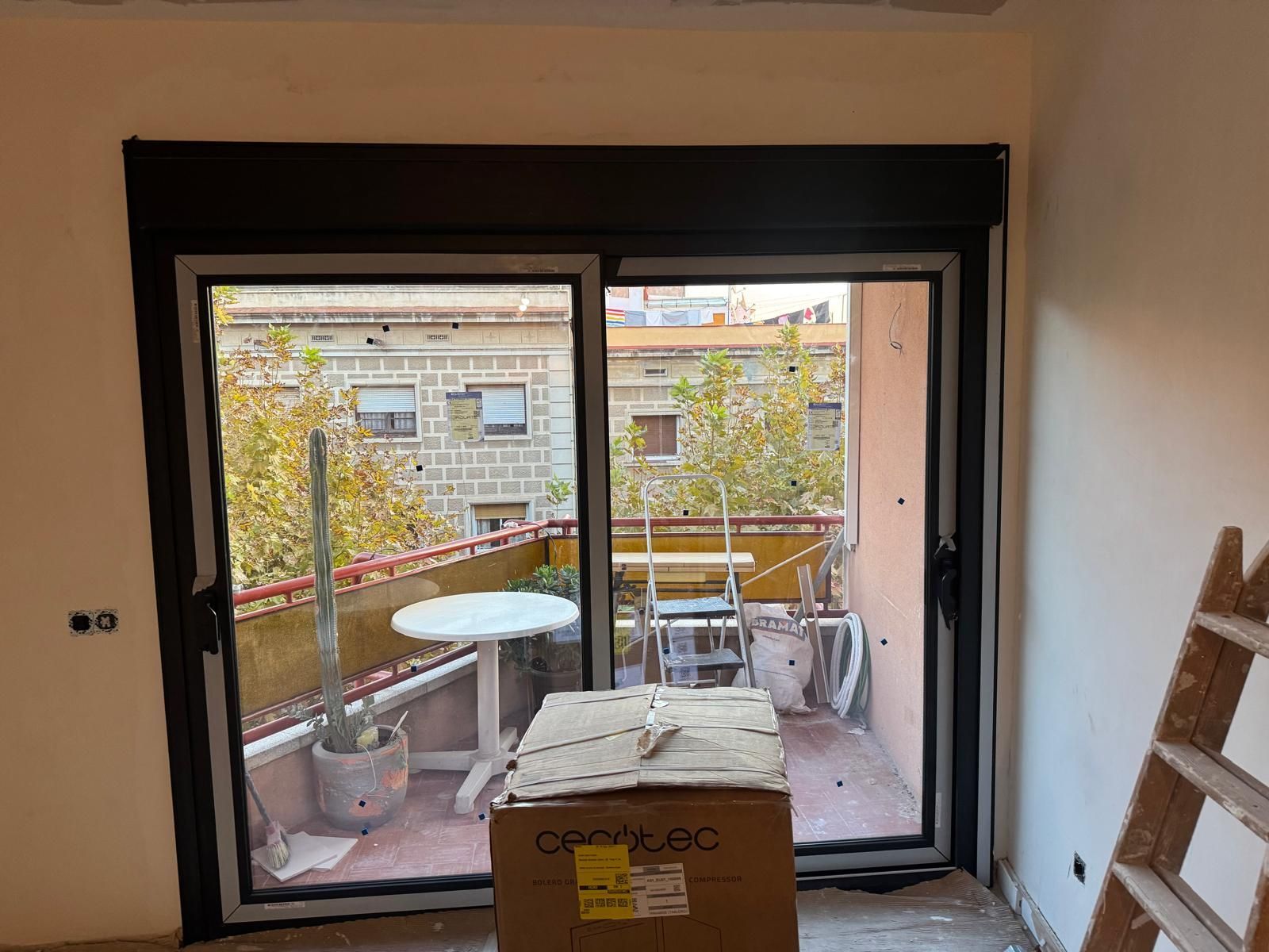 Unas puertas correderas de cristal dan acceso a un pequeño balcón con macetas y una jardinera en su interior.