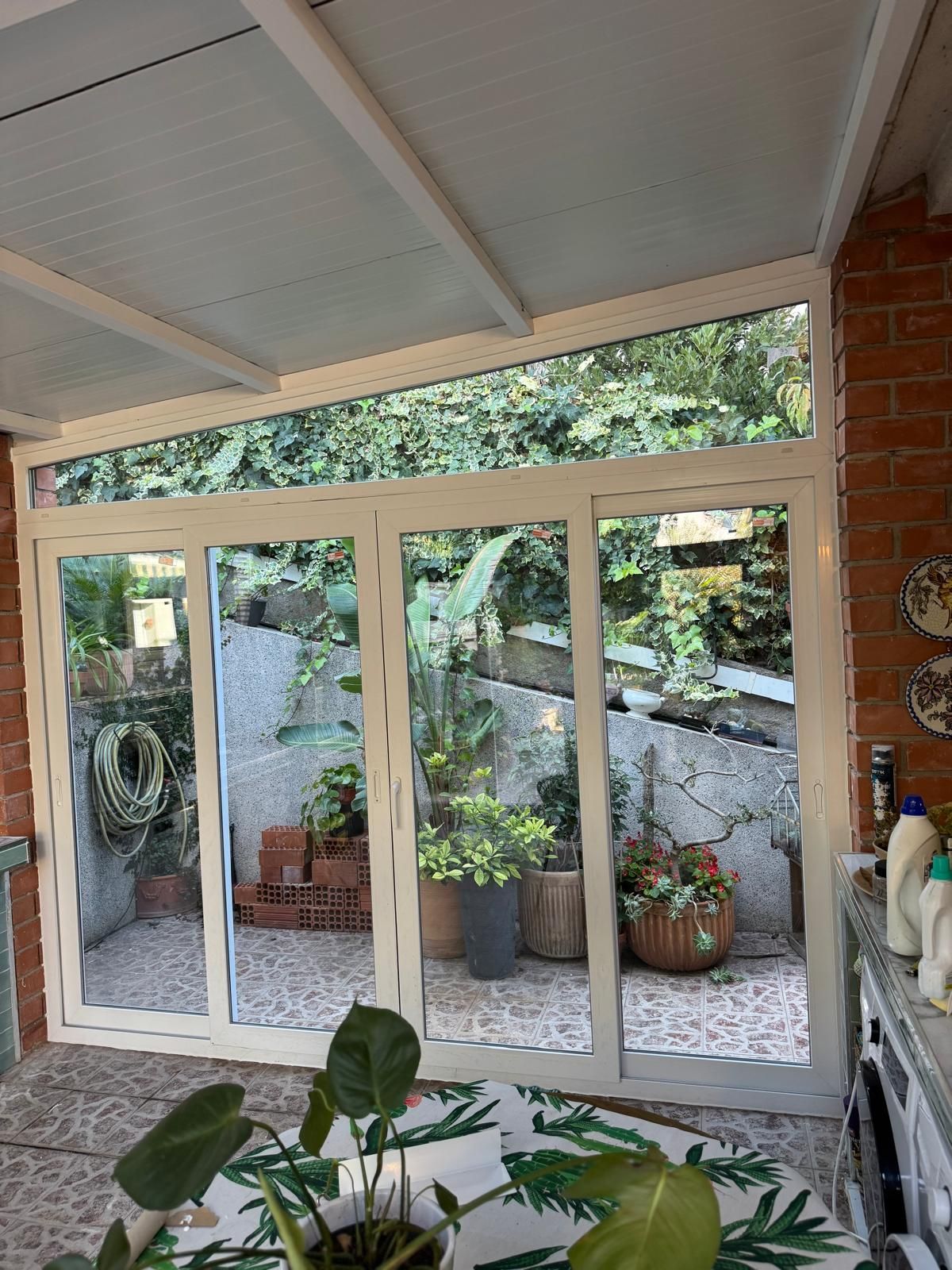 Patio cubierto con grandes puertas corredizas de vidrio que dan a un pequeño patio ajardinado.