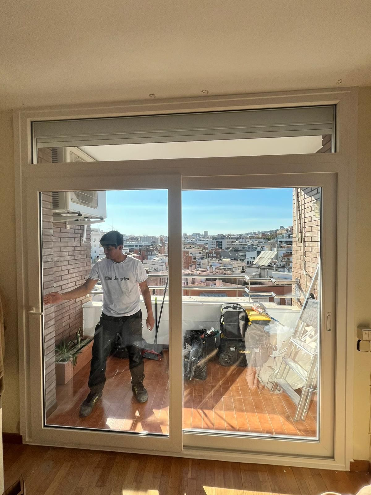 Una persona se encuentra en un balcón detrás de unas puertas de cristal, con vistas a la ciudad y al agua.