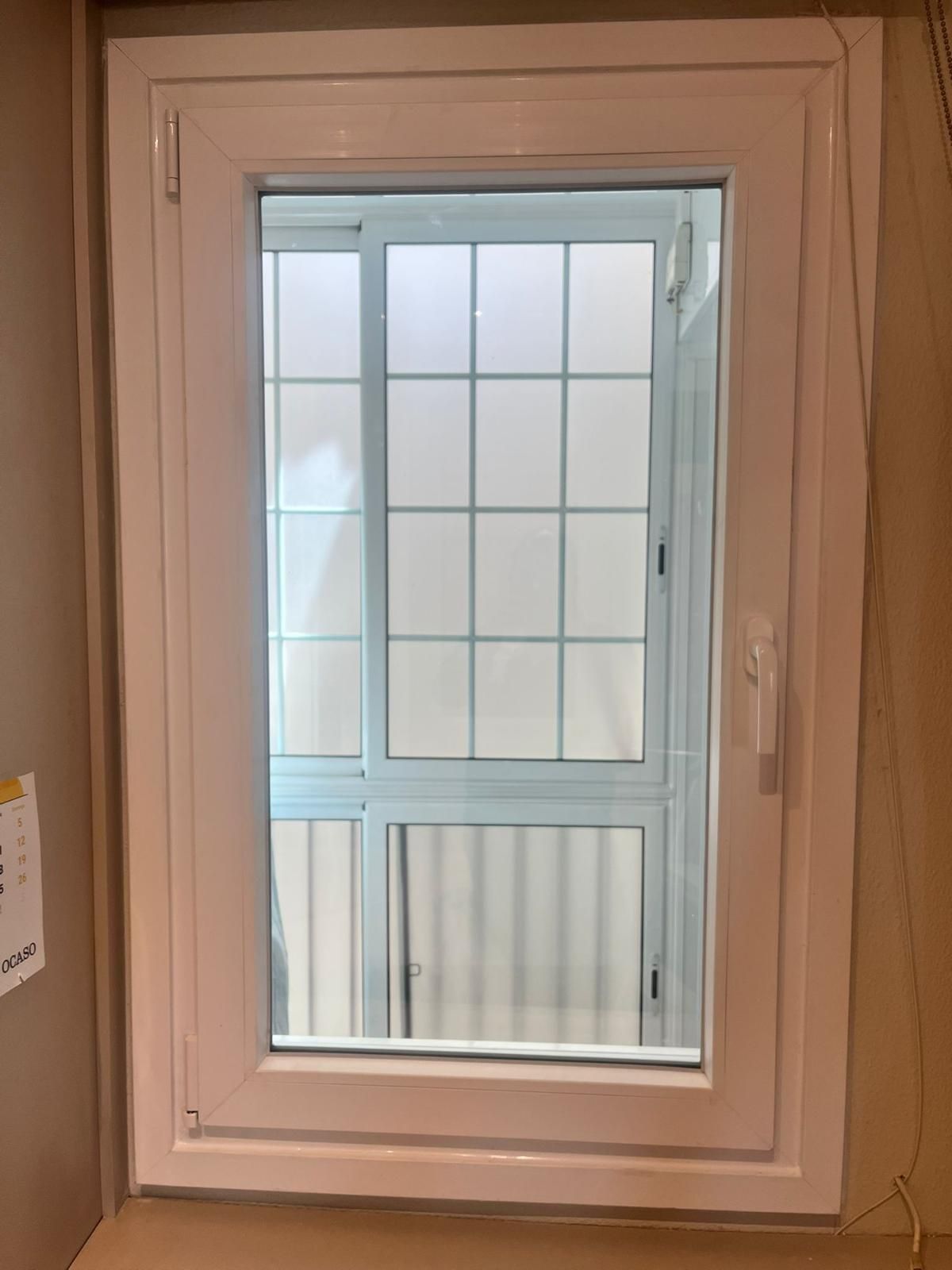 Pequeña ventana con marco blanco en una pared beige, que deja ver una cuadrícula de cristales y la luz del exterior.