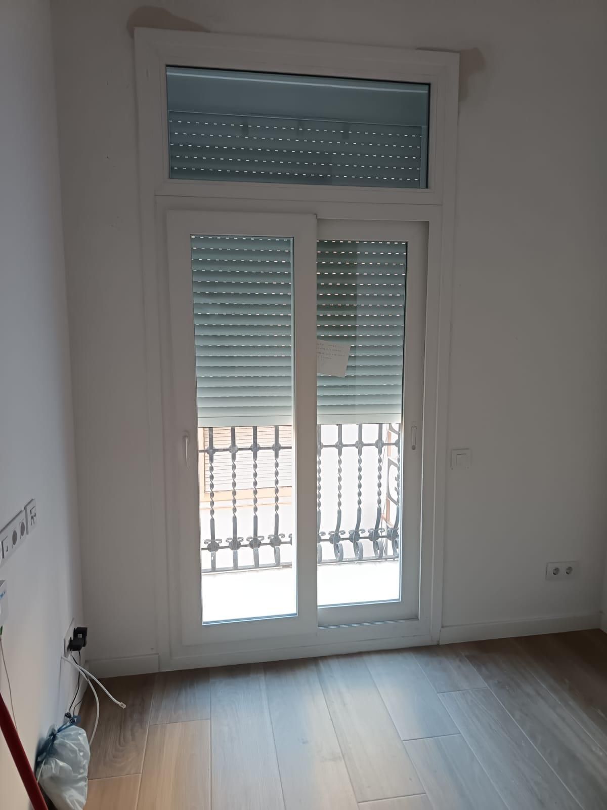 Habitación vacía con puertas francesas blancas, contraventanas y suelo de madera clara.