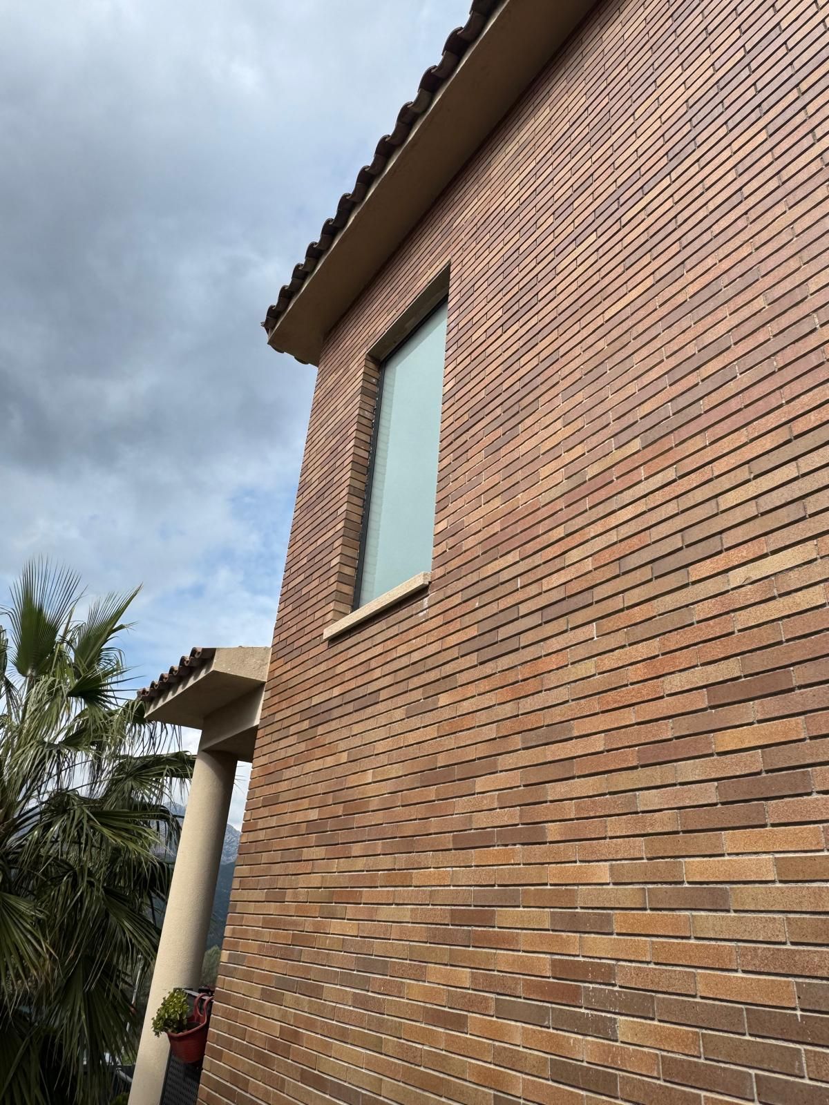 Exterior de una casa de ladrillo con una ventana alta bajo un cielo nublado.