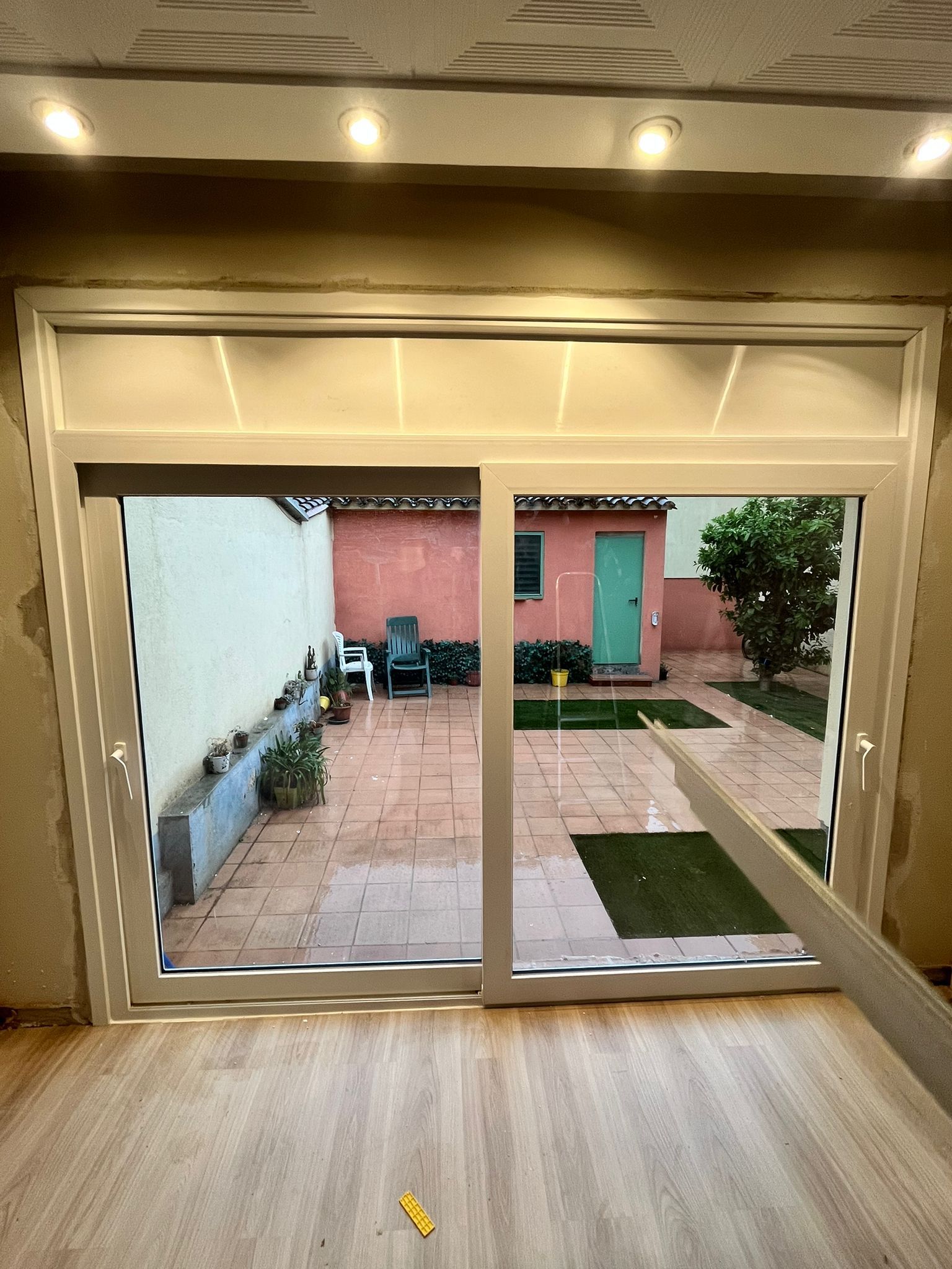 Unas puertas corredizas de cristal dan acceso a un pequeño patio con adoquines, sillas y, al fondo, una puerta rosa.