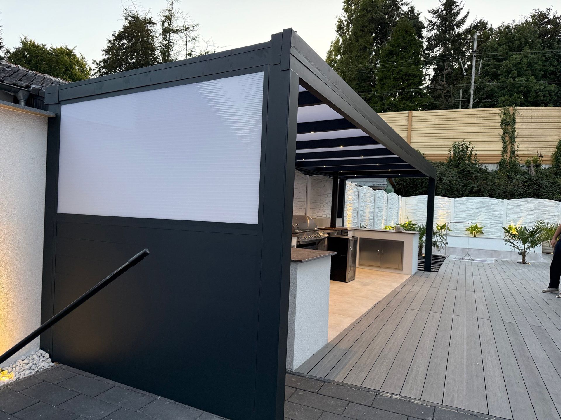 Dunkelgraue Pergola für die Außenküche mit weißer, durchscheinender Seitenwand.