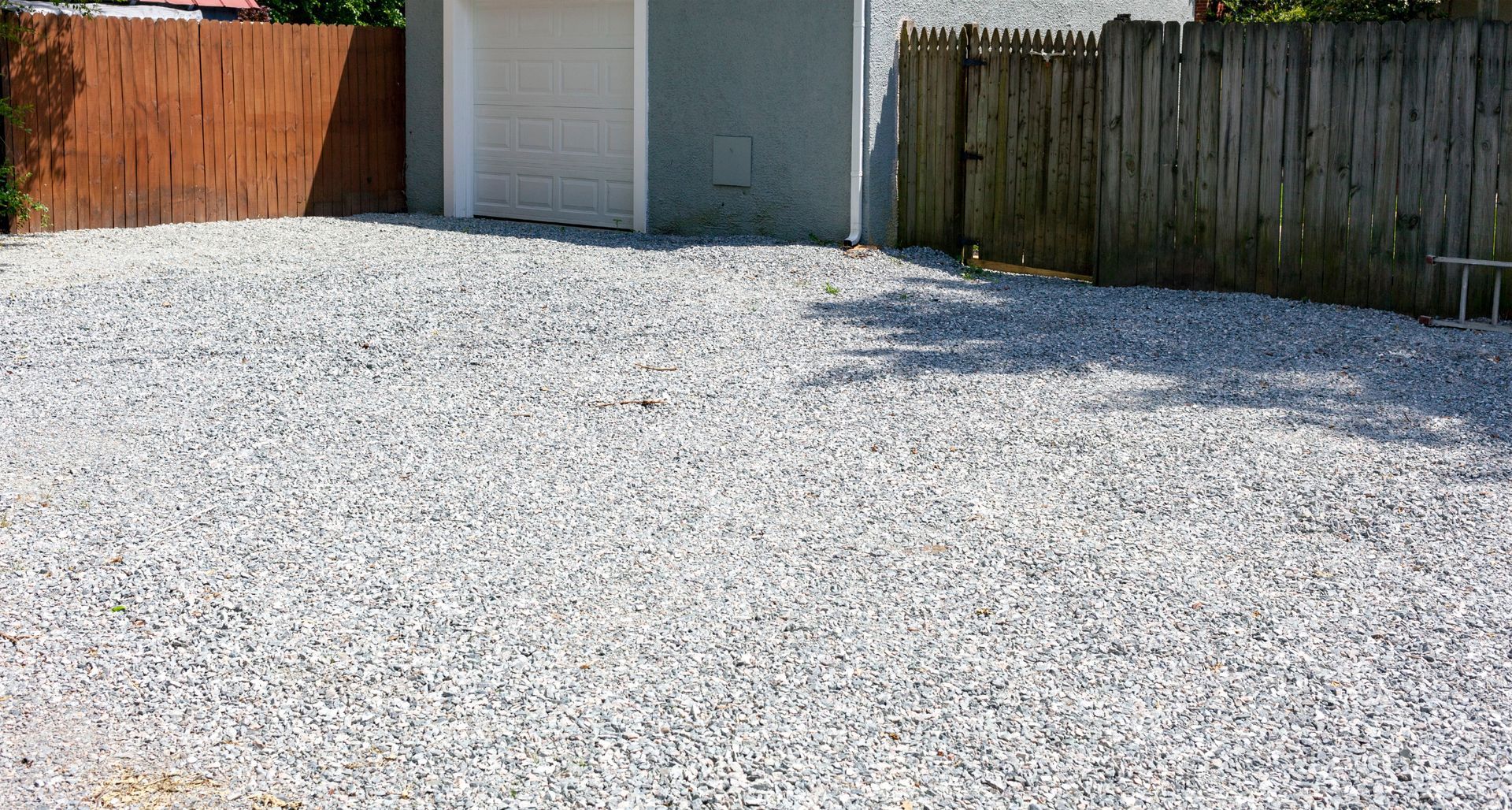 Allée de gravier entre une clôture en bois et un garage avec une porte de garage blanche.