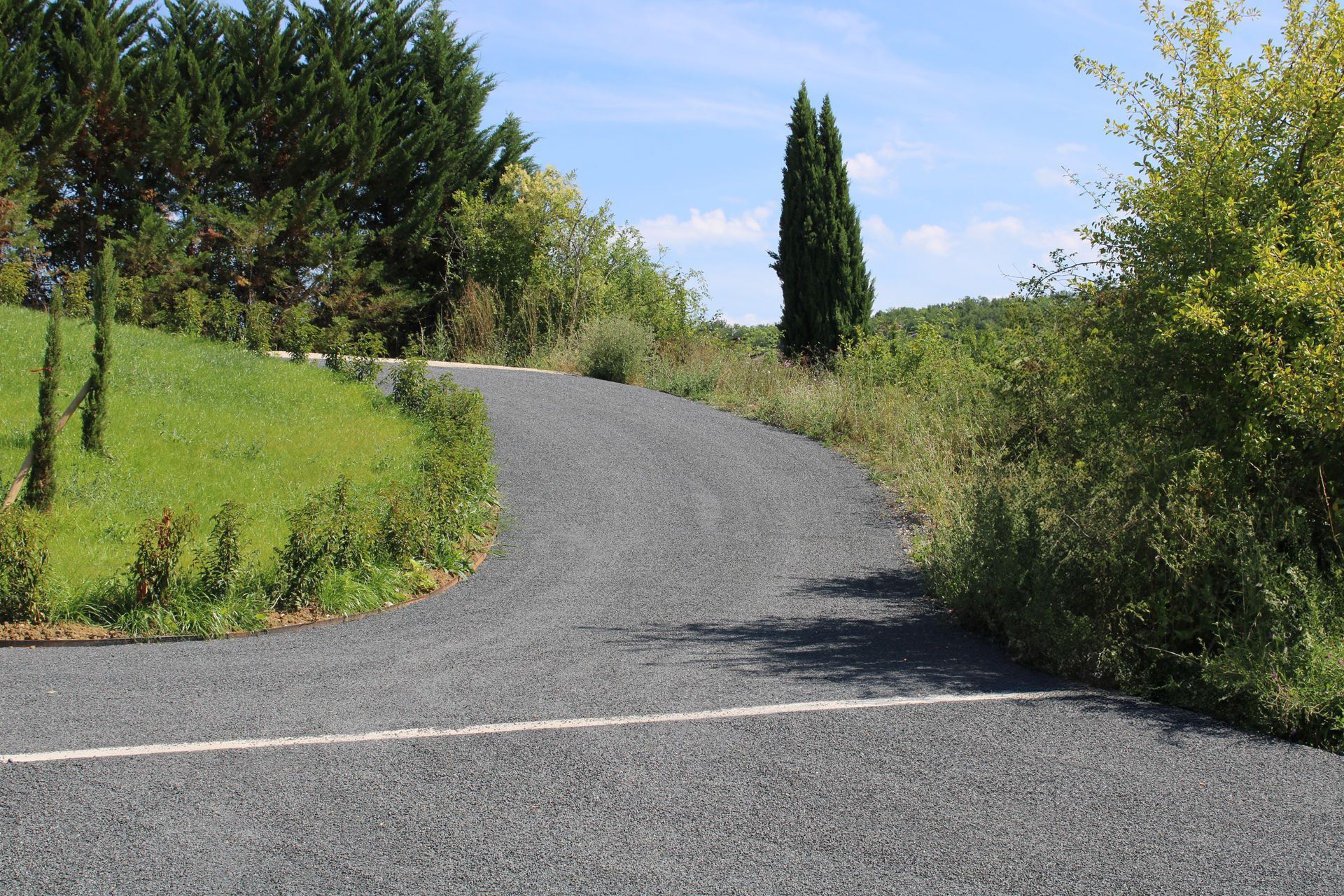 Chemin de gravier sinueux serpentant entre des arbustes et des arbres verdoyants sous un ciel bleu