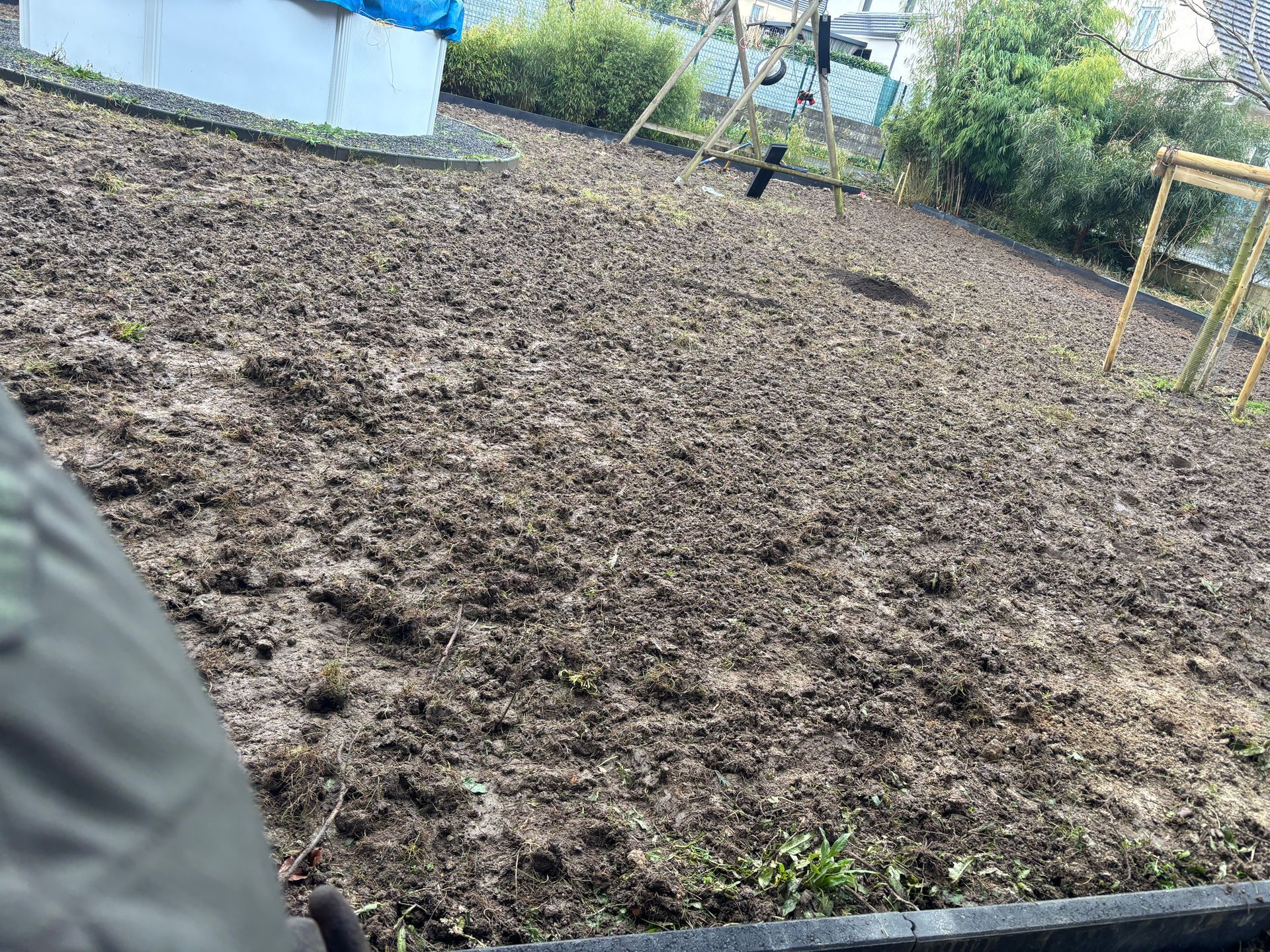 Un grand parterre de jardin labouré dans une cour, avec une balançoire et du feuillage en arrière-plan.