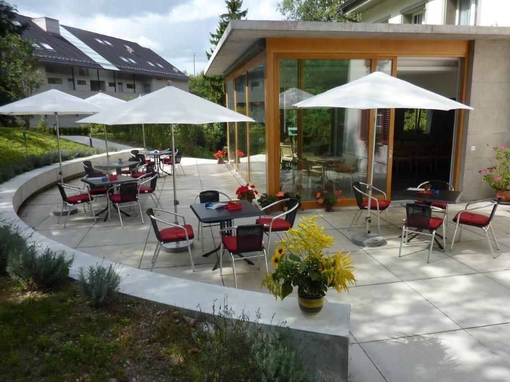 Eine Terrasse mit Tischen, Stühlen und Sonnenschirmen vor einem Gebäude