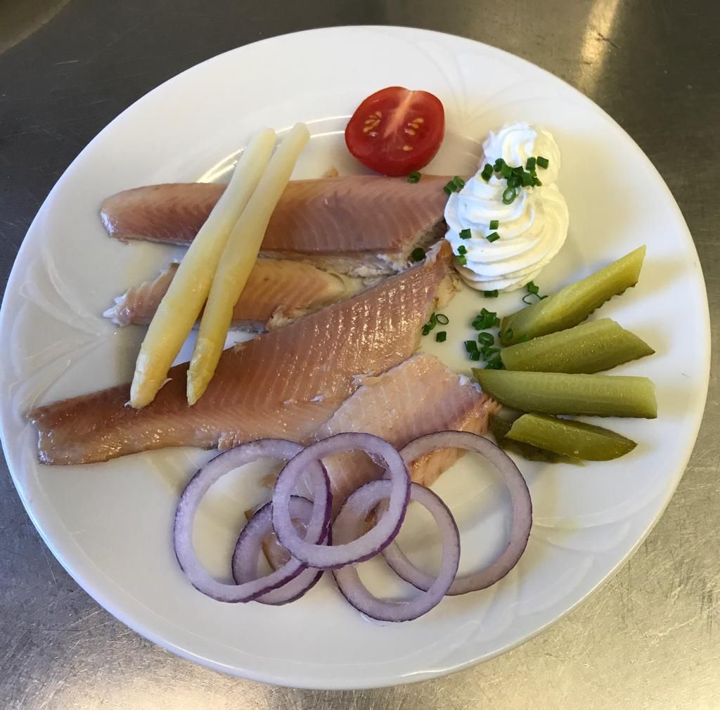 Ein weißer Teller mit Fisch, Spargel, Zwiebeln und Gurken