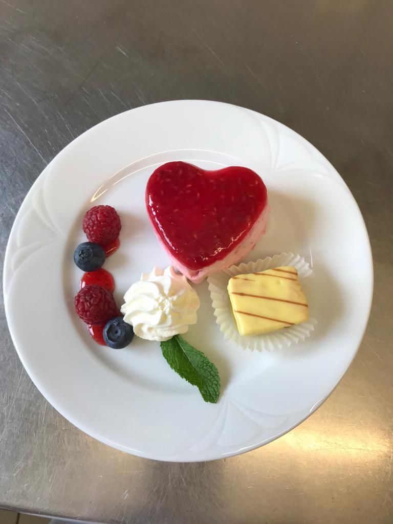 Ein weißer Teller mit einem herzförmigen Dessert und Beeren.