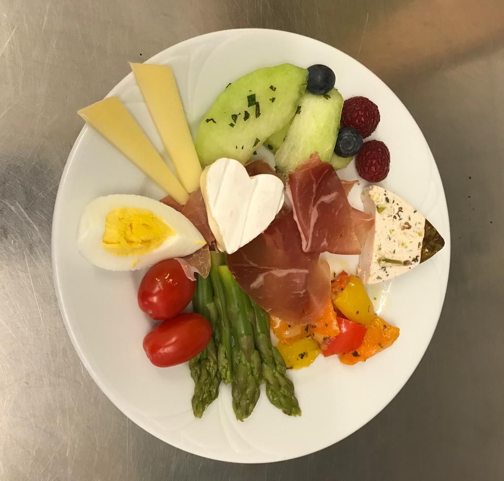 Ein weißer Teller mit Eiern, Spargel, Käse und Obst